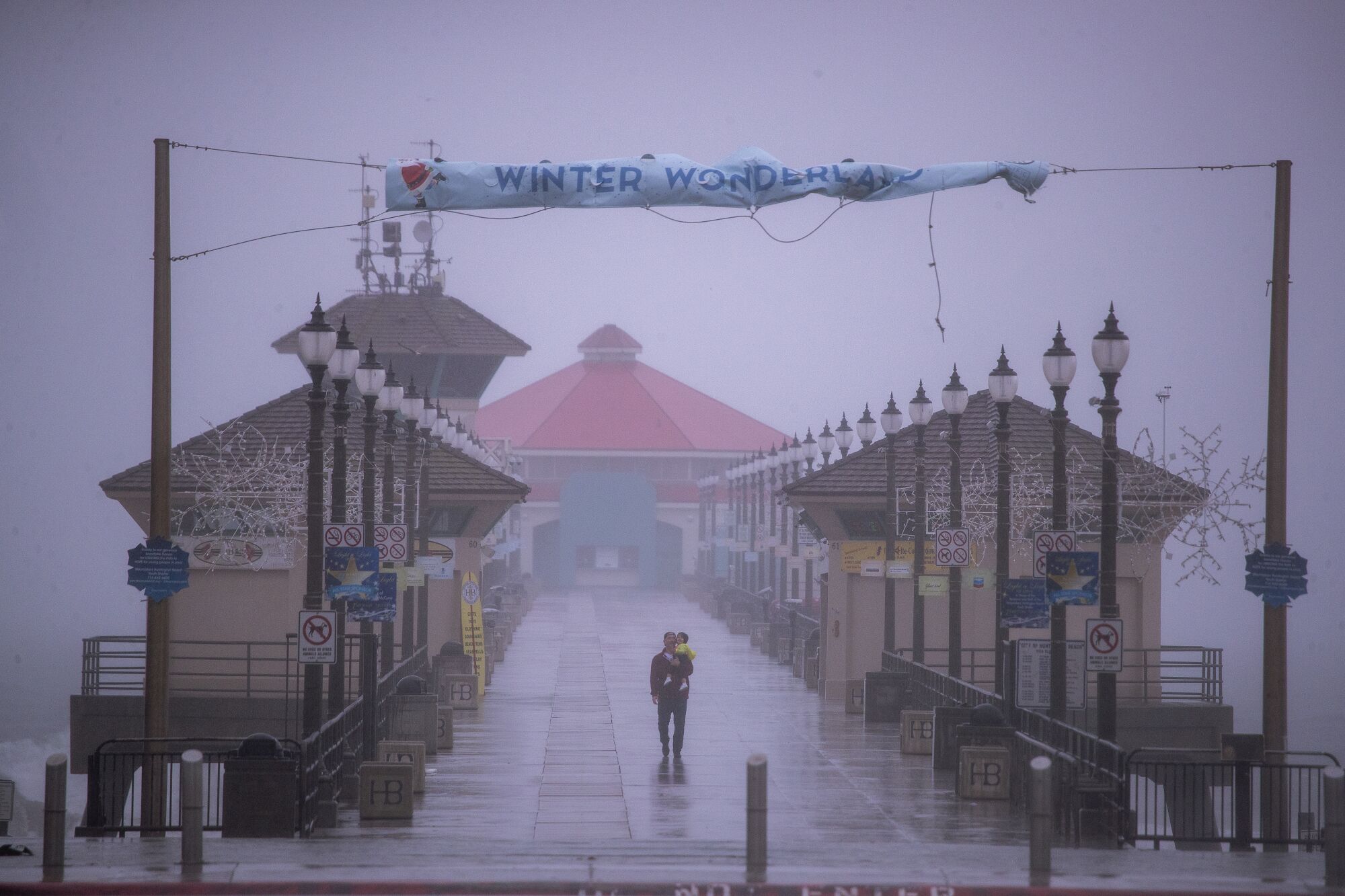 Under a "Winter Wonderland" banner, a man and child walk in solitude down the Huntington Beach Pier.