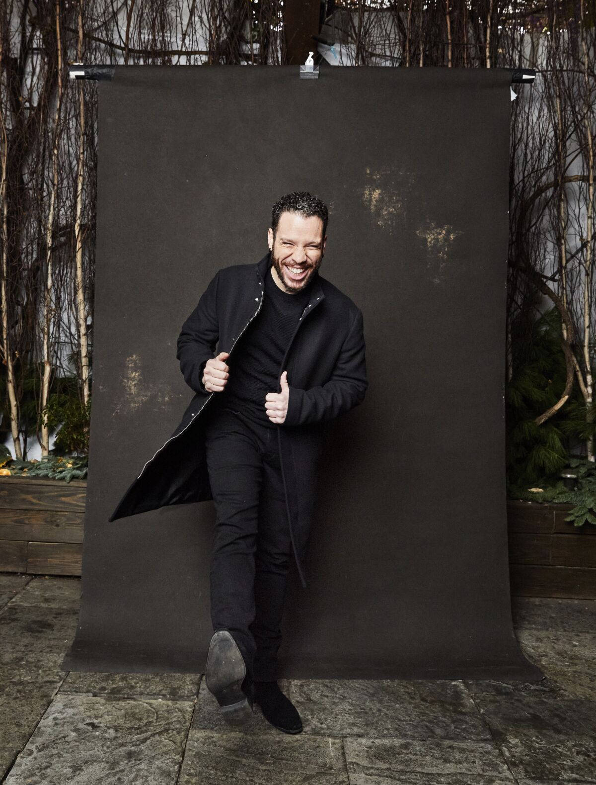 Actor Robin de Jesus, dressed in all black, kicks a leg up in front of a black backdrop.