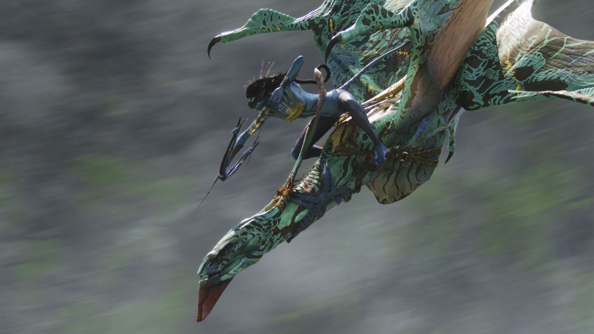 A blue human-like creature aims an arrow while standing on a large bird-like creature in flight in "Avatar" 