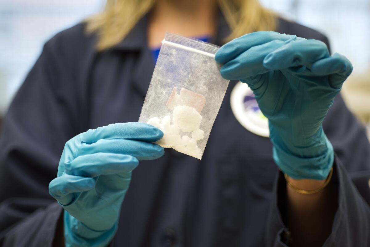 A person wearing gloves holds up a small bag of fentanyl.