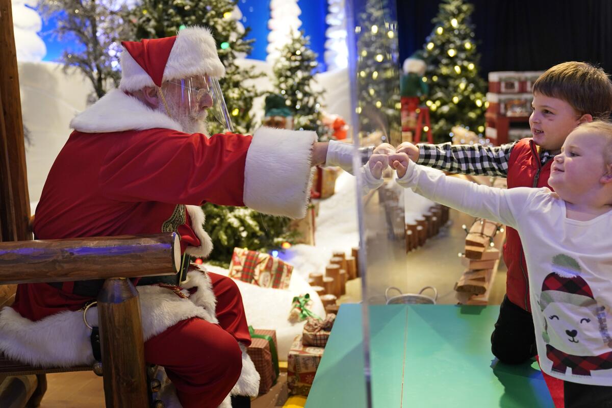 Julianna, 3, and Dylan, 5, Lasczak visit with Santa through a transparent barrier at a Bass Pro Shop in Bridgeport, Conn., Tuesday, Nov. 10, 2020. Santa Claus is coming to the mall — just don't try to sit on his lap. Malls are doing all they can to keep the jolly old man safe from the coronavirus, including banning kids from sitting on his knee, no matter if they've been naughty or nice. (AP Photo/Seth Wenig)