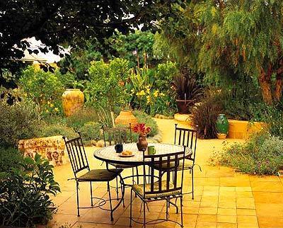 Apricot and California pepper trees shelter a dining terrace paved with French limestone. Nearby the designer planted hellebores, daylilies, red fountain grass, cannas and Spanish lavender.