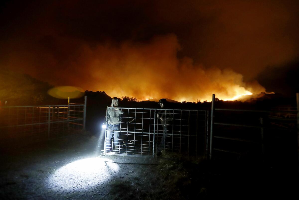 Near Healdsburg, Calif., a pair of men open a gate to allow firefighters access to a ranch along State Highway 128 as the Kincade fire flares up early Sunday.