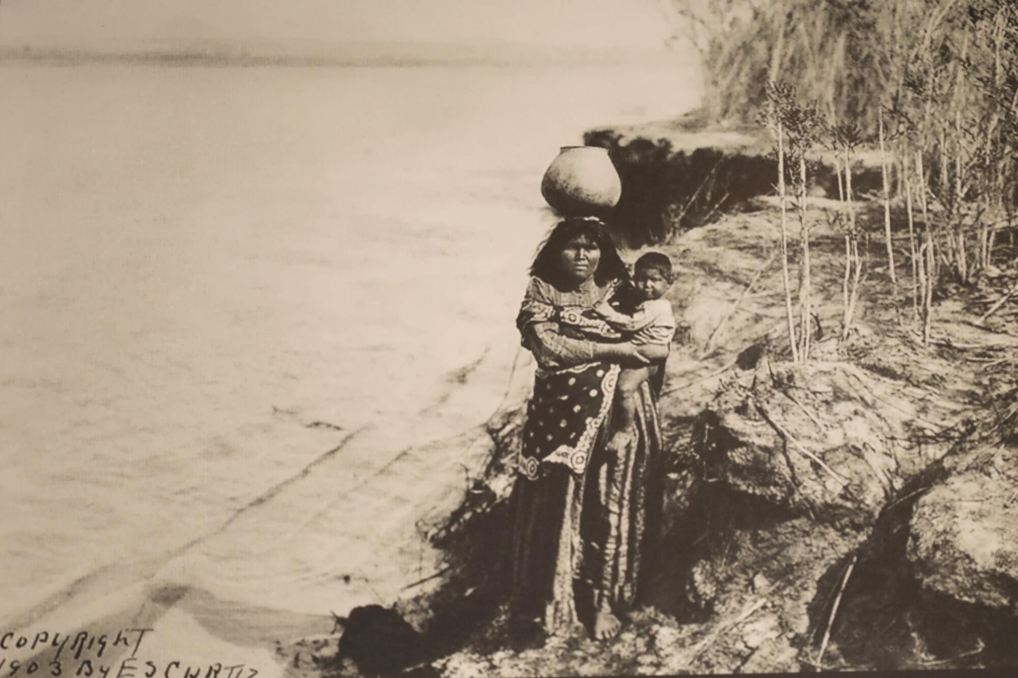 An old photo shows a woman holding a baby along a river