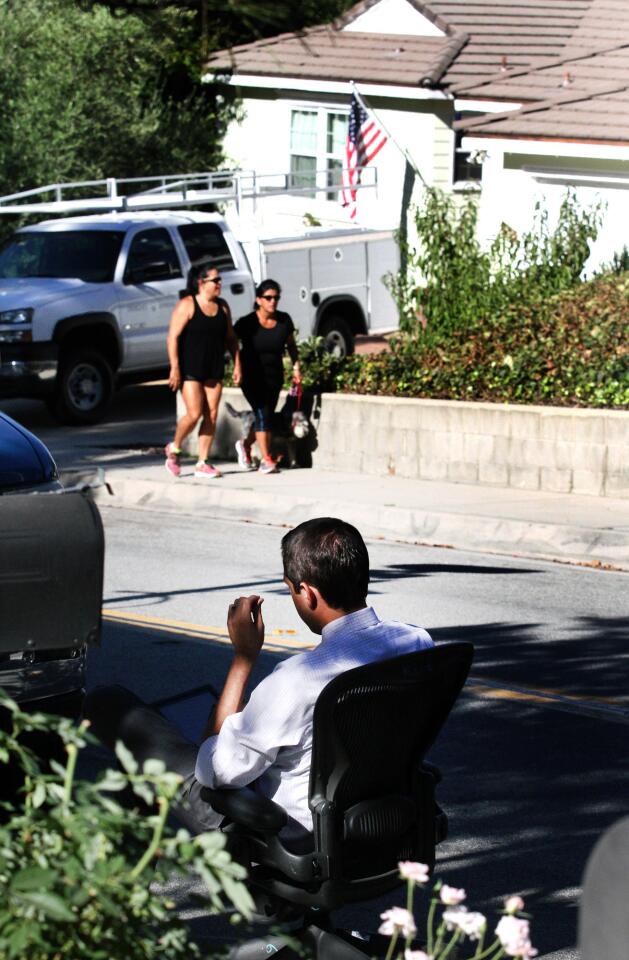 Channel 7's Marc Cota Robles sits in an office chair on the side of the street as neighbors walk past the the scene of a murder-suicide on the 5000 block of Crown Avenue in La Cañada Flintridge on Monday, Sept. 7, 2015. On Sunday night, a 5-year veteran of the Los Angeles County Fire Department shot and killed his wife, a 2-year veteran of the Sheriff's Department. He then killed himself at a county Fire Department facility in Pacoima, according to officials.