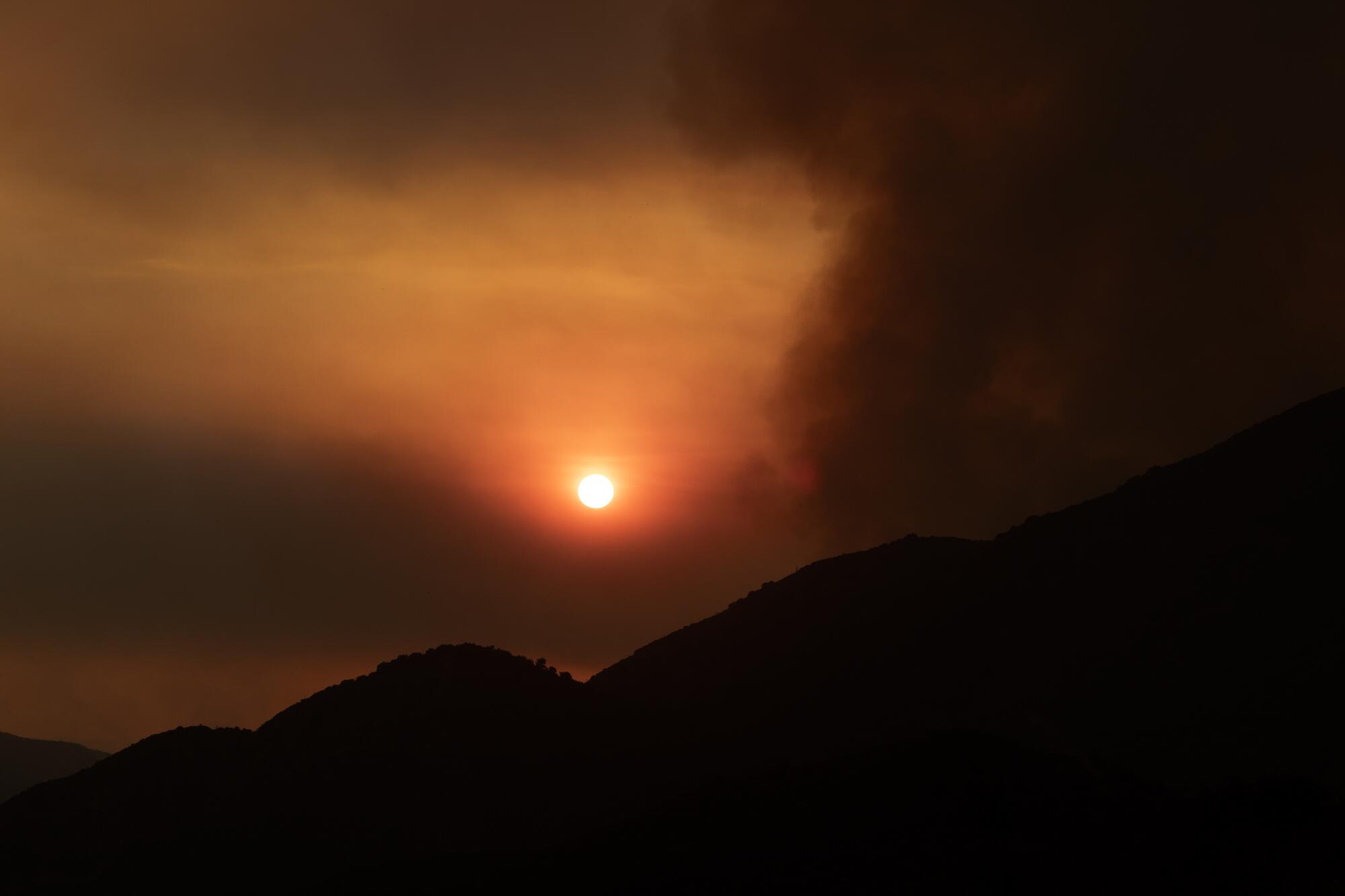 Wildfire smoke obscures the sun and turns the sky an ominous hue of orange.