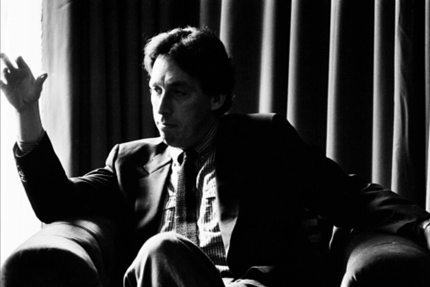 A man sitting in a chair gestures with his hand in a black and white photo