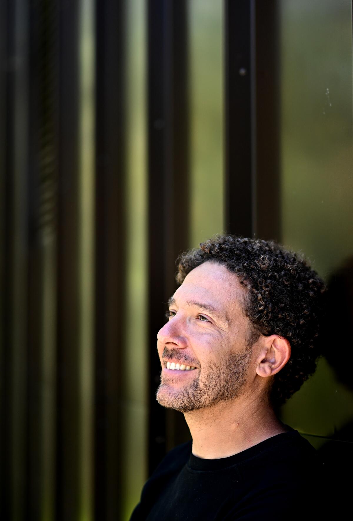 A smiling man is seen in a close-up portrait against a green geometric background.