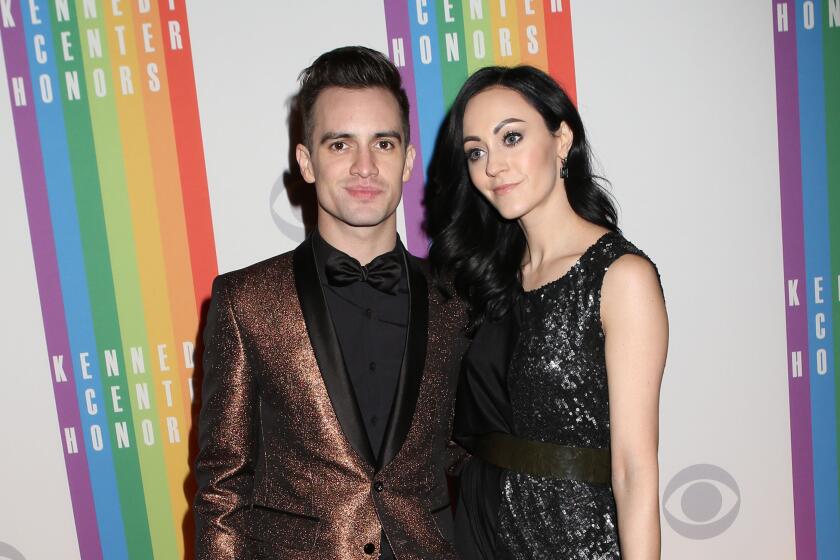 A man in a copper suit and a dark-haired woman in a dark gown pose on a red carpet