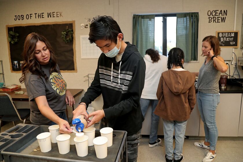 TeacherOs aid April Lancaster, left, guides senior Kevin Luu, 18, center, in measuring coffee creamer as they fill orders at Ocean View High School on Friday morning in Huntington Beach. (Kevin Chang / Daily Pilot)