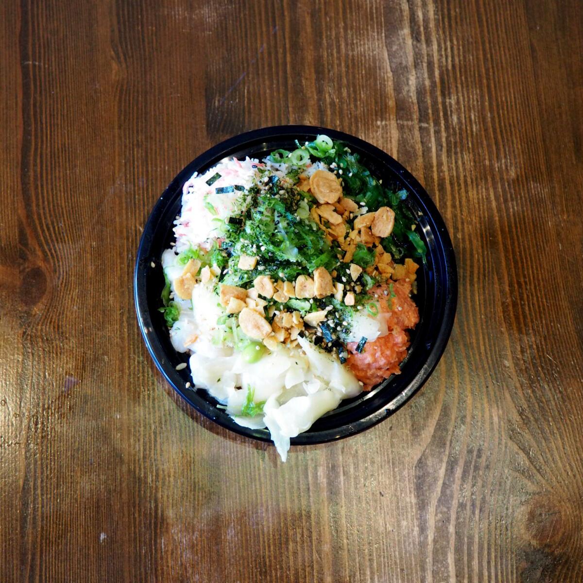 A spicy tuna and scallop poke bowl with brown rice, green onion, pickled ginger, seaweed salad, imitation crab, sesame seeds and furikake.