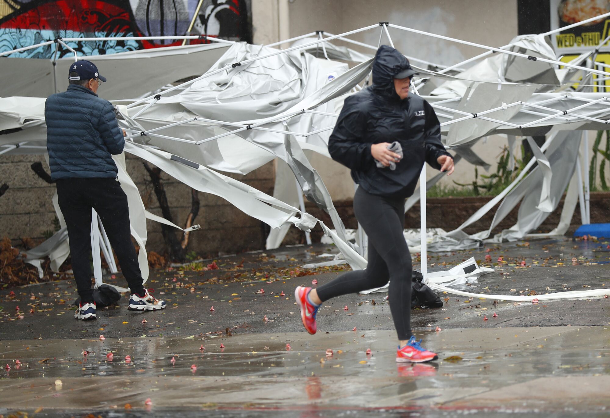 A jogger runs by a worker cleaning up the top to a canopy that blew apart at a Pacific Beach restaurant in high winds.