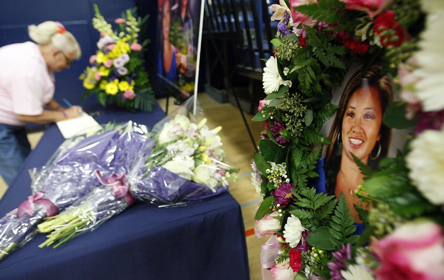 A mourner signs a condolence book for slain Cal State Fullerton assistant women's basketball coach Monica Quan, pictured at right, before a home game against UC Irvine on Saturday. Quan and her fiance are believed to be the first victims of a fatal shooting rampage by fired LAPD officer Christopher Jordan Dorner.