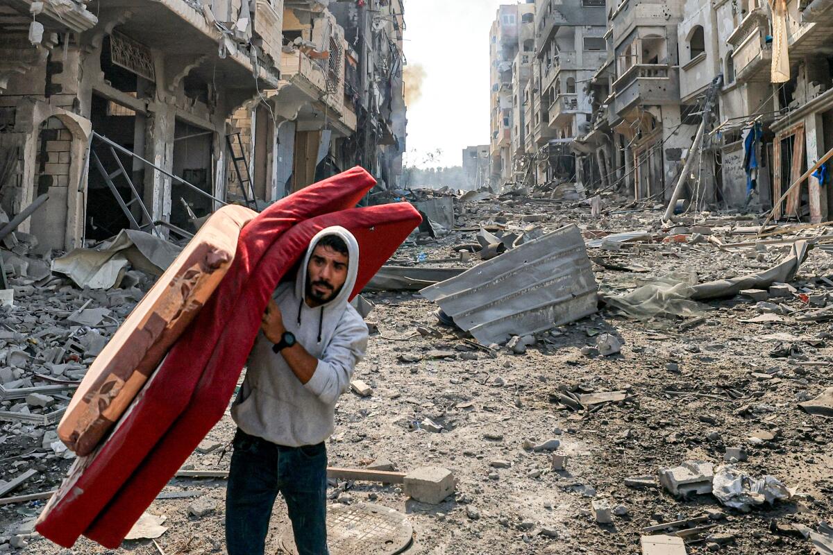 A man carries salvaged bedding on a rubble-filled street 