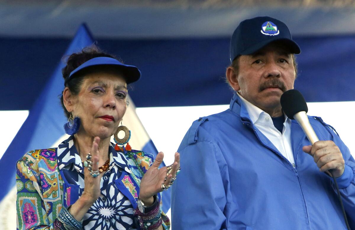 A woman in a patterned jacket and shirt, left, and a man holding a microphone