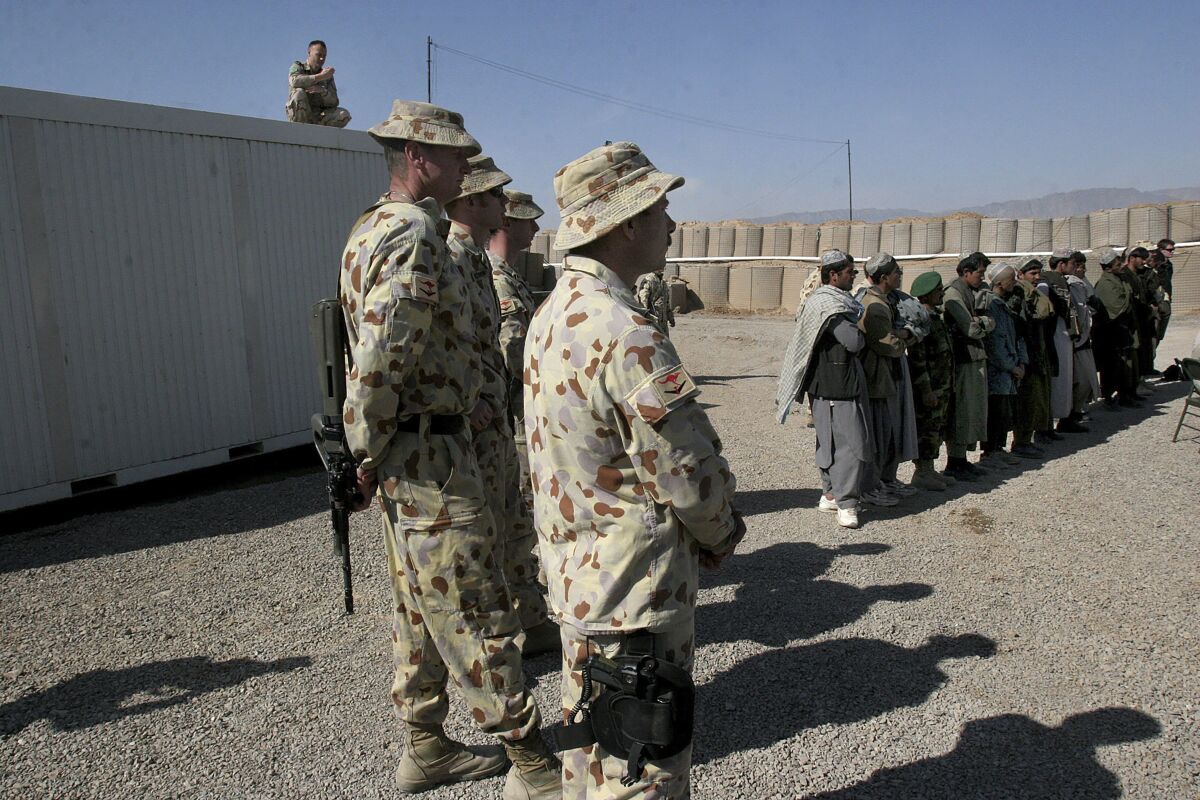 FILE - In this Feb. 17, 2007 file, Australian soldiers, part of the International Security Assistance Force (ISAF), stand near local Afghans at a ceremony to open a Trade Training School, funded by Australian forces at the Tarin Kowt military base in Uruzgan province, south of Kabul, Afghanistan. An Afghan army deserter who murdered three Australian soldiers had been released from custody in Qatar and his whereabouts were not known, officials said on Monday, Oct. 11, 2021. (AP Photo/Musadeq Sadeq, File)