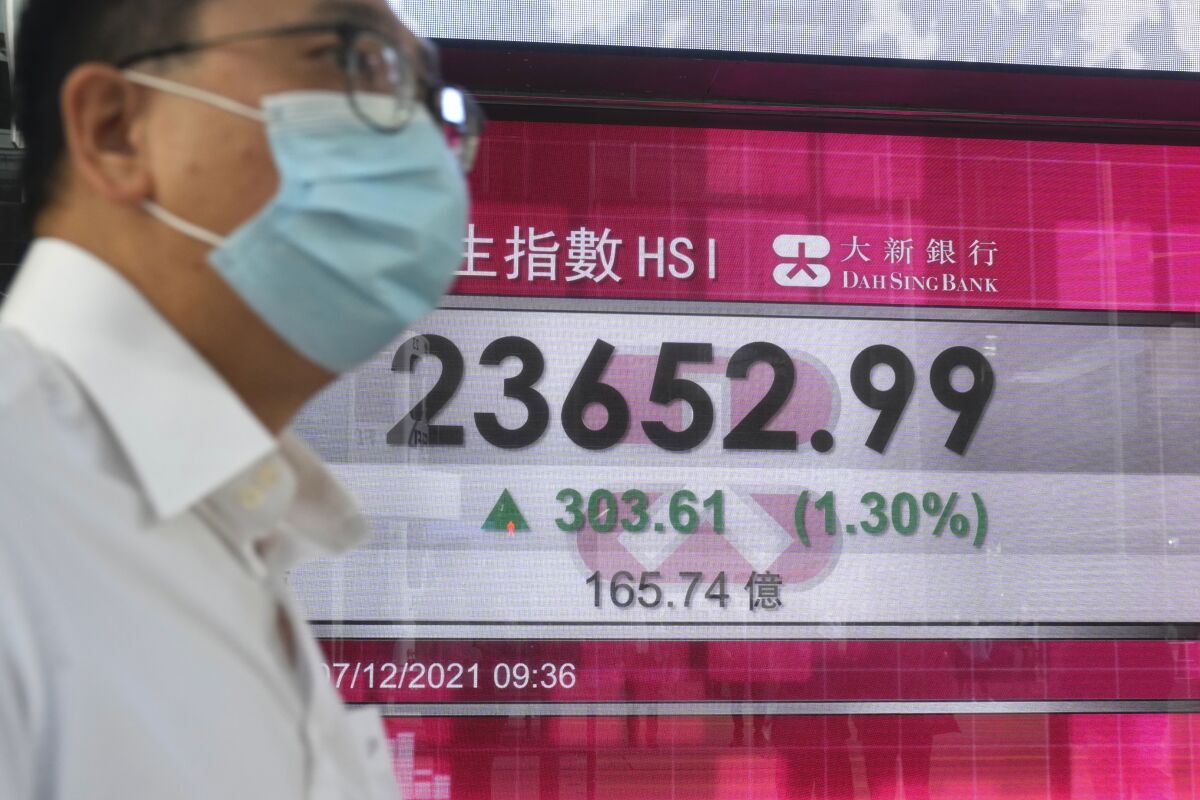 A man wearing a face mask walks past a bank's electronic board showing the Hong Kong share index in Hong Kong, Tuesday, Dec. 7, 2021. Asia stock markets followed Wall Street higher Tuesday as anxiety about the coronavirus's latest variant eased. (AP Photo/Kin Cheung)