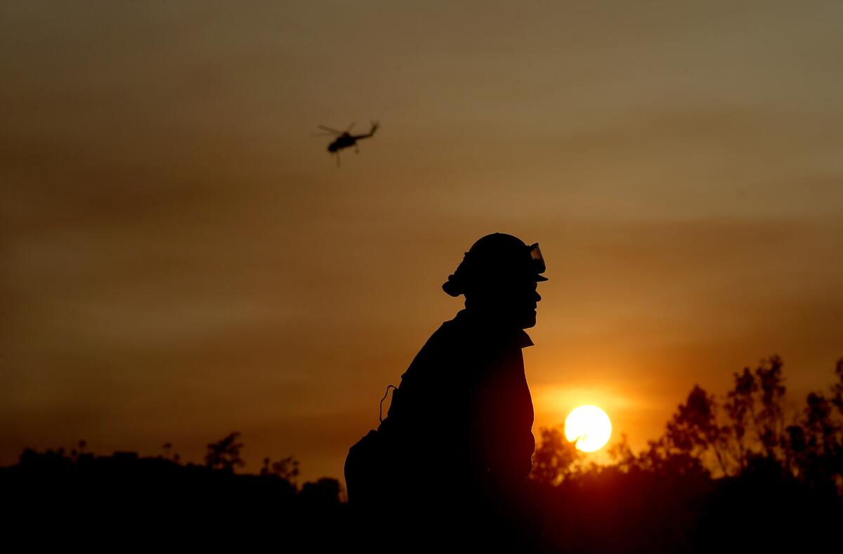 The sun sets behind a firefighter working along Country Club Drive in Escondido on Thursday evening as wildfires continued to burn in San Diego County.
