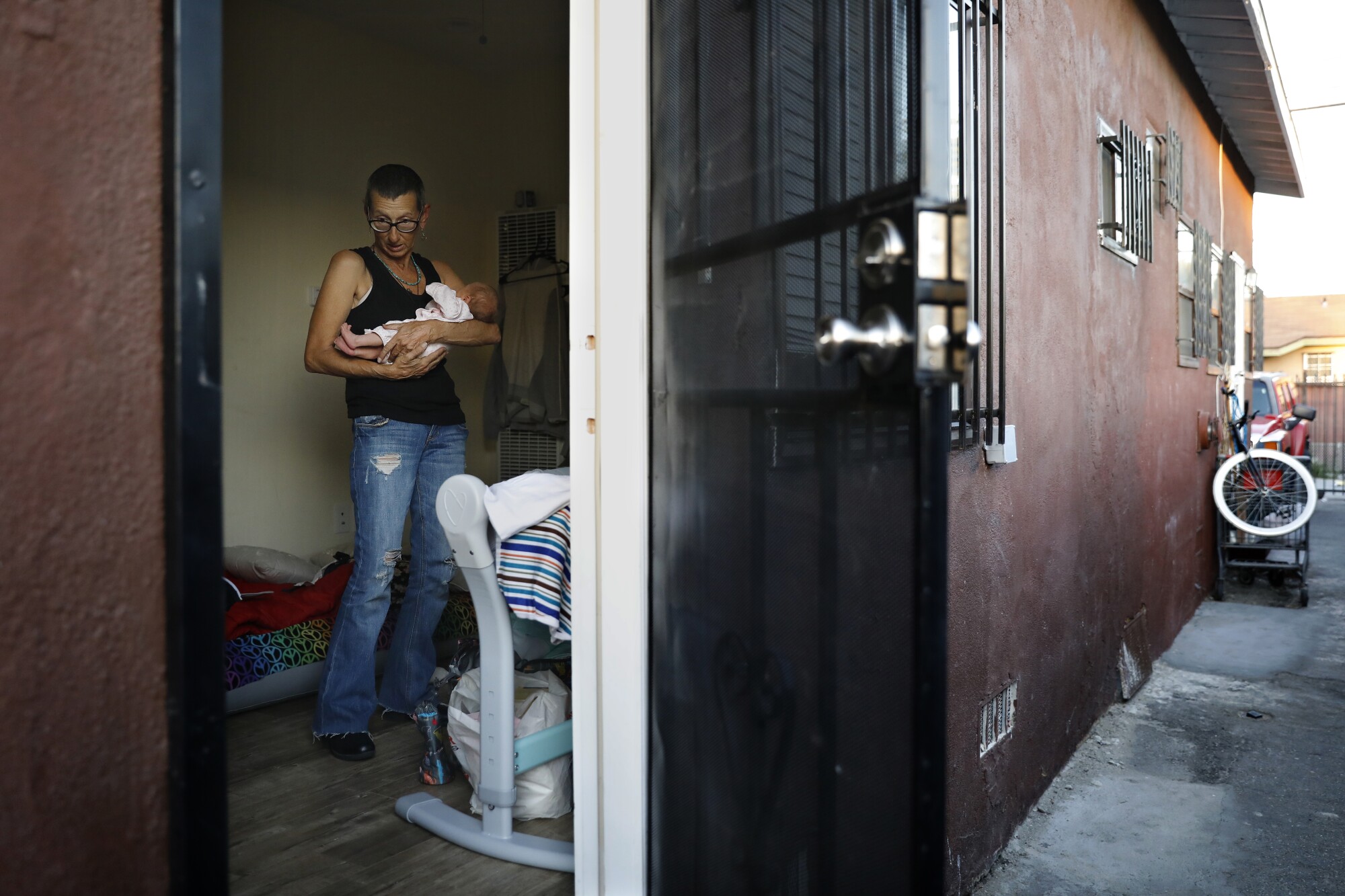 A woman holds a baby visible through an open door of an apartment.