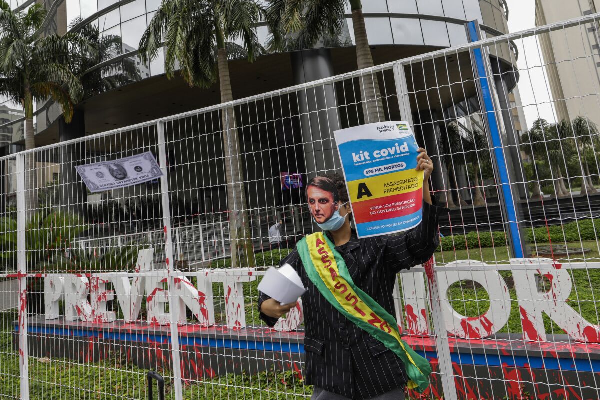 A demonstrator in a Brazilian President Jair Bolsonaro mask protests against the Prevent Senior health care company outside its headquarters in Sao Paulo, Brazil, Sept. 30, 2021. Whistleblowing doctors, through their lawyer, testified at the Senate last week that Prevent Senior enlisted participants to test unproven drugs without proper consent and forced doctors to toe the line on prescribing unproven drugs touted by President Jair Bolsonaro as part of a “COVID kit,” in the treatment of the new coronavirus. (AP Photo/Marcelo Chello)