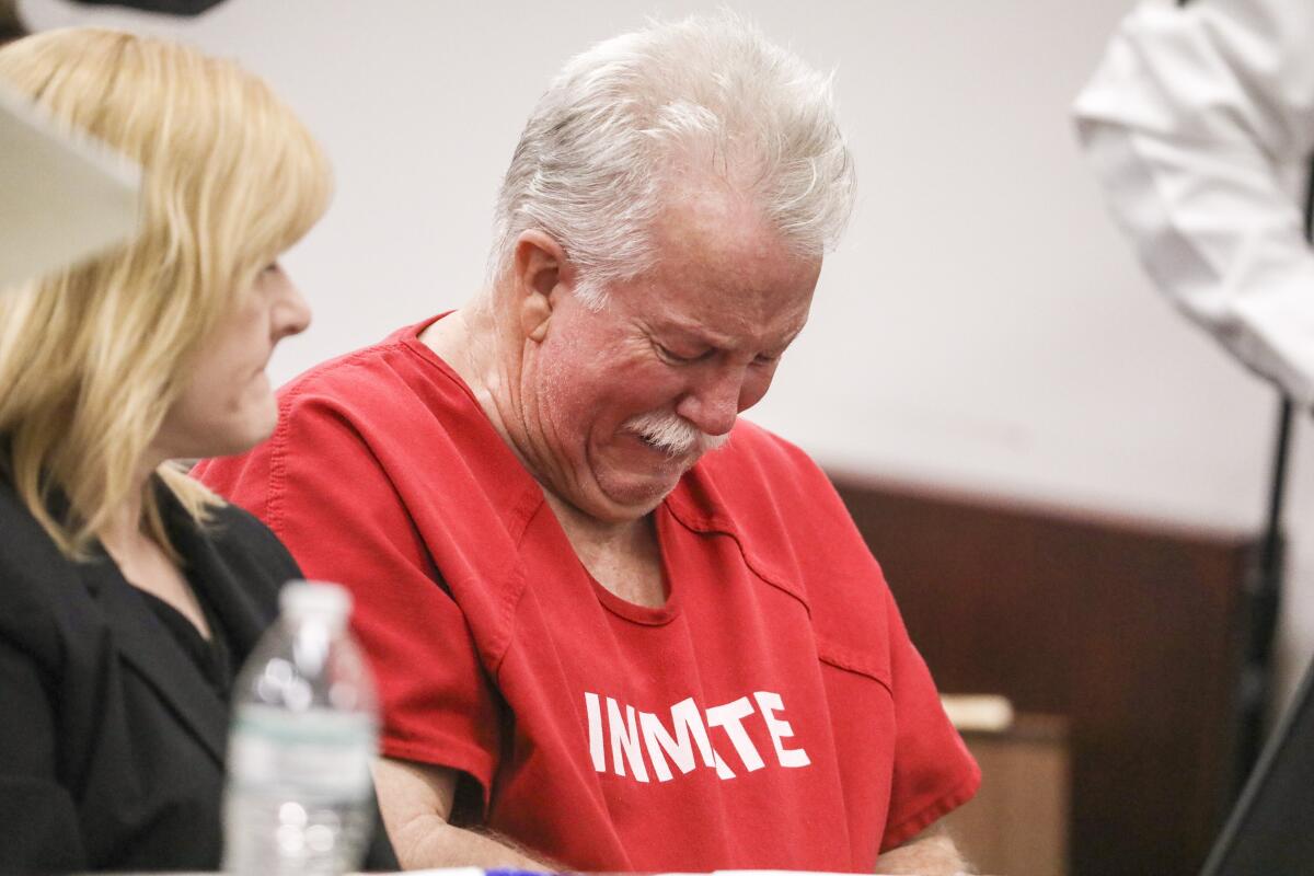 A man in a red jail jumpsuit bows his head and cries