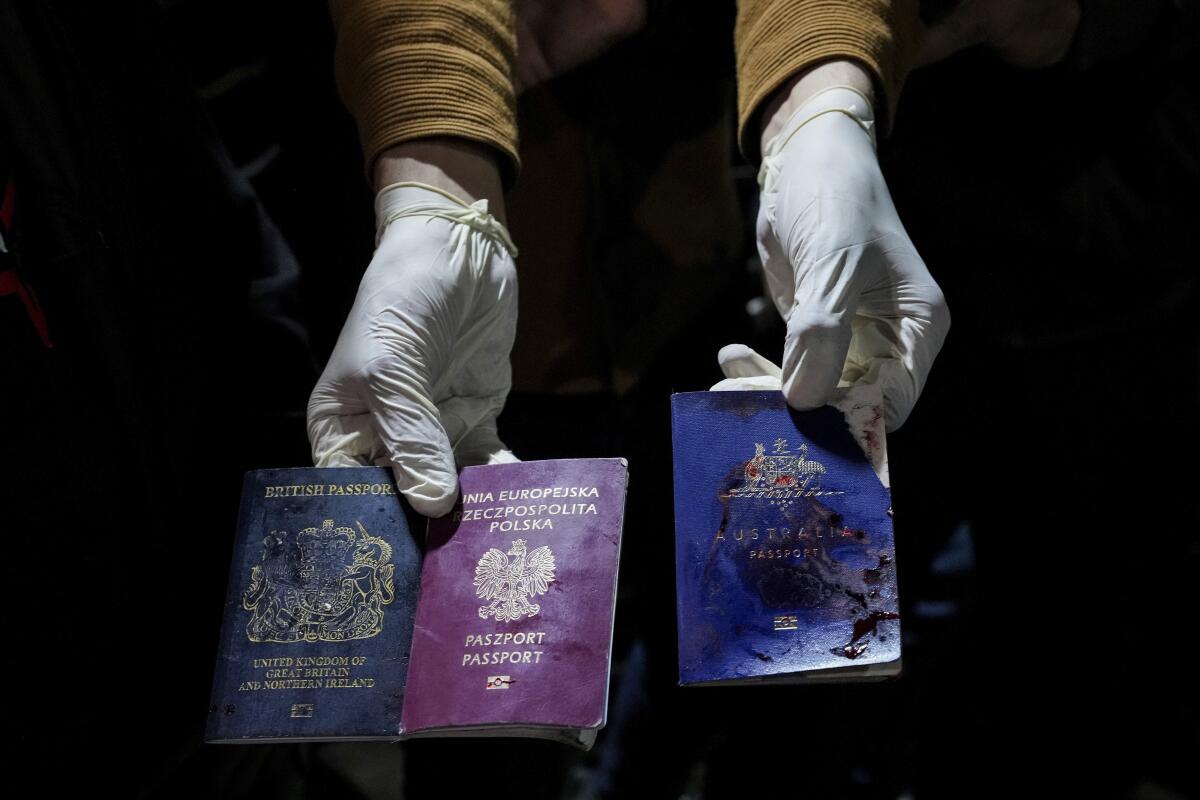 Hands wearing gloves hold bloodstained British, Polish and Australian passports.