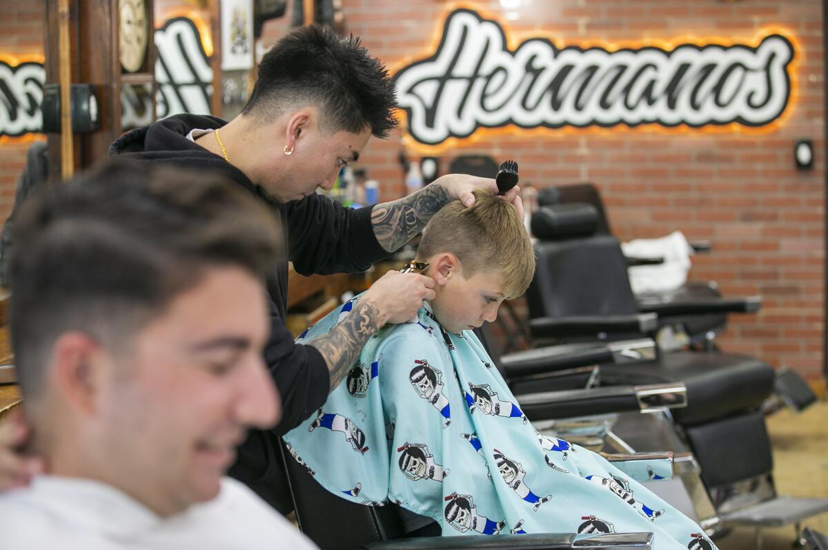 Barbers cut hair at Hermanos Barbershop in Huntington Beach on Monday, two days after a burglary there. 