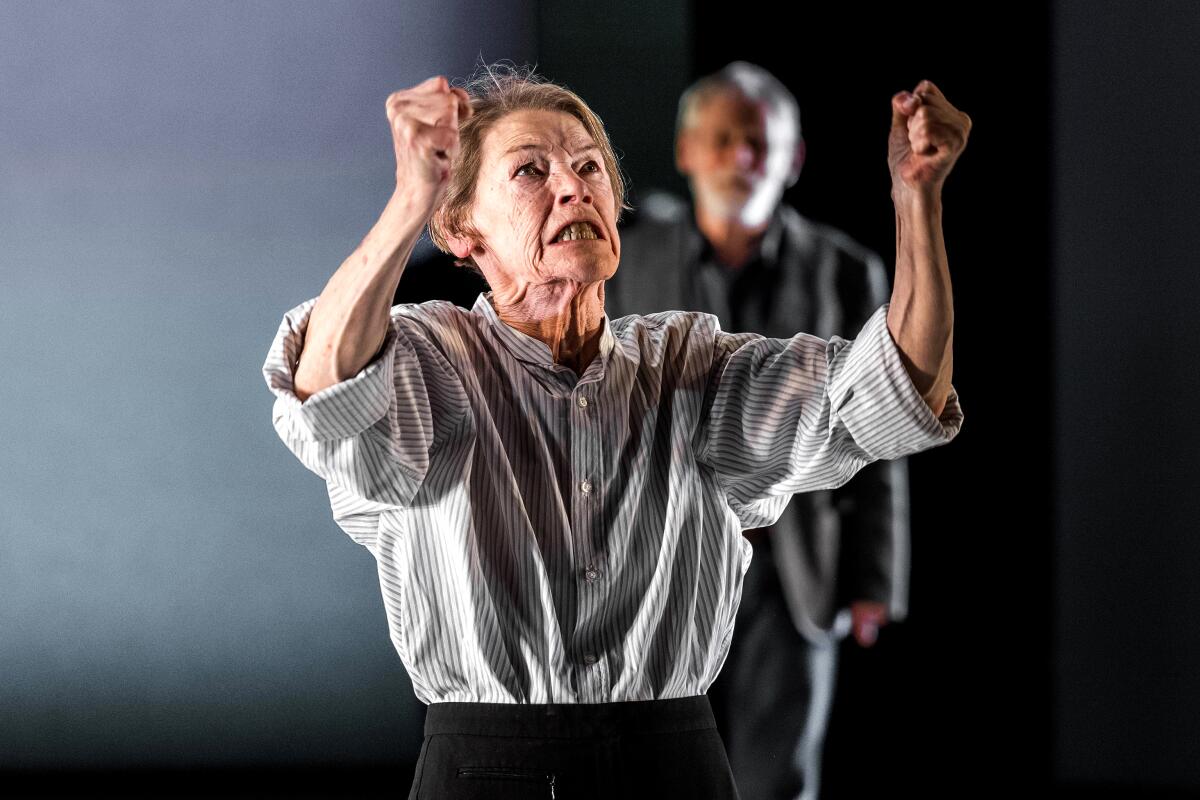 Glenda Jackson in shirt and trousers shakes her fists at the sky.