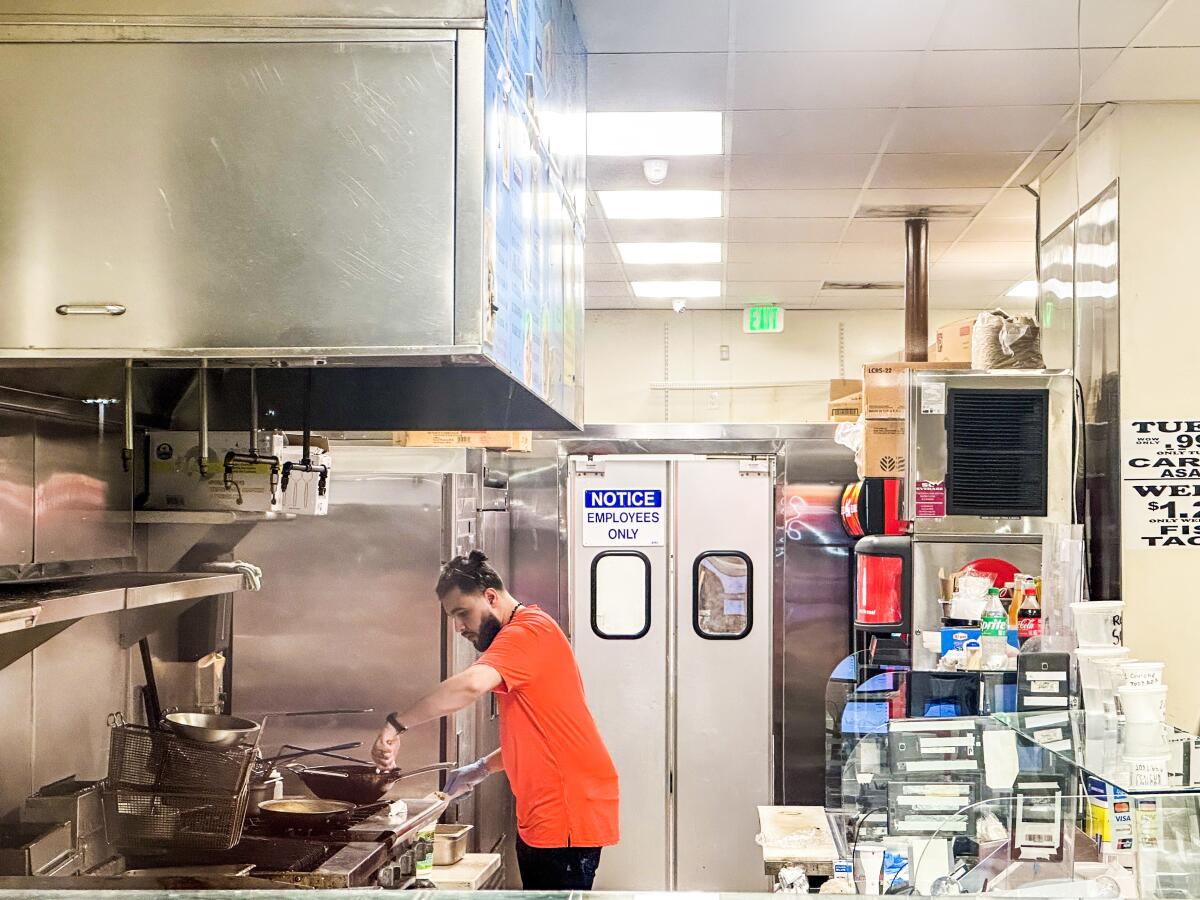 A man in an orange T-shirt works in a restaurant kitchen