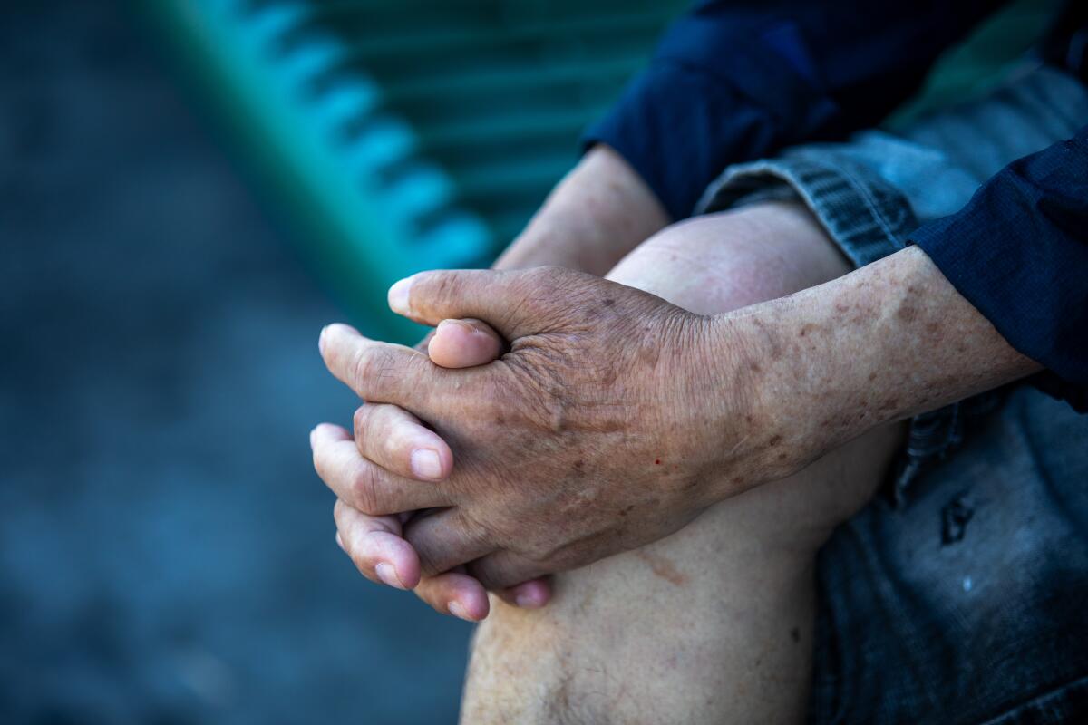 A man clasps his hands on his knee while waiting for a bus in Koreatown.