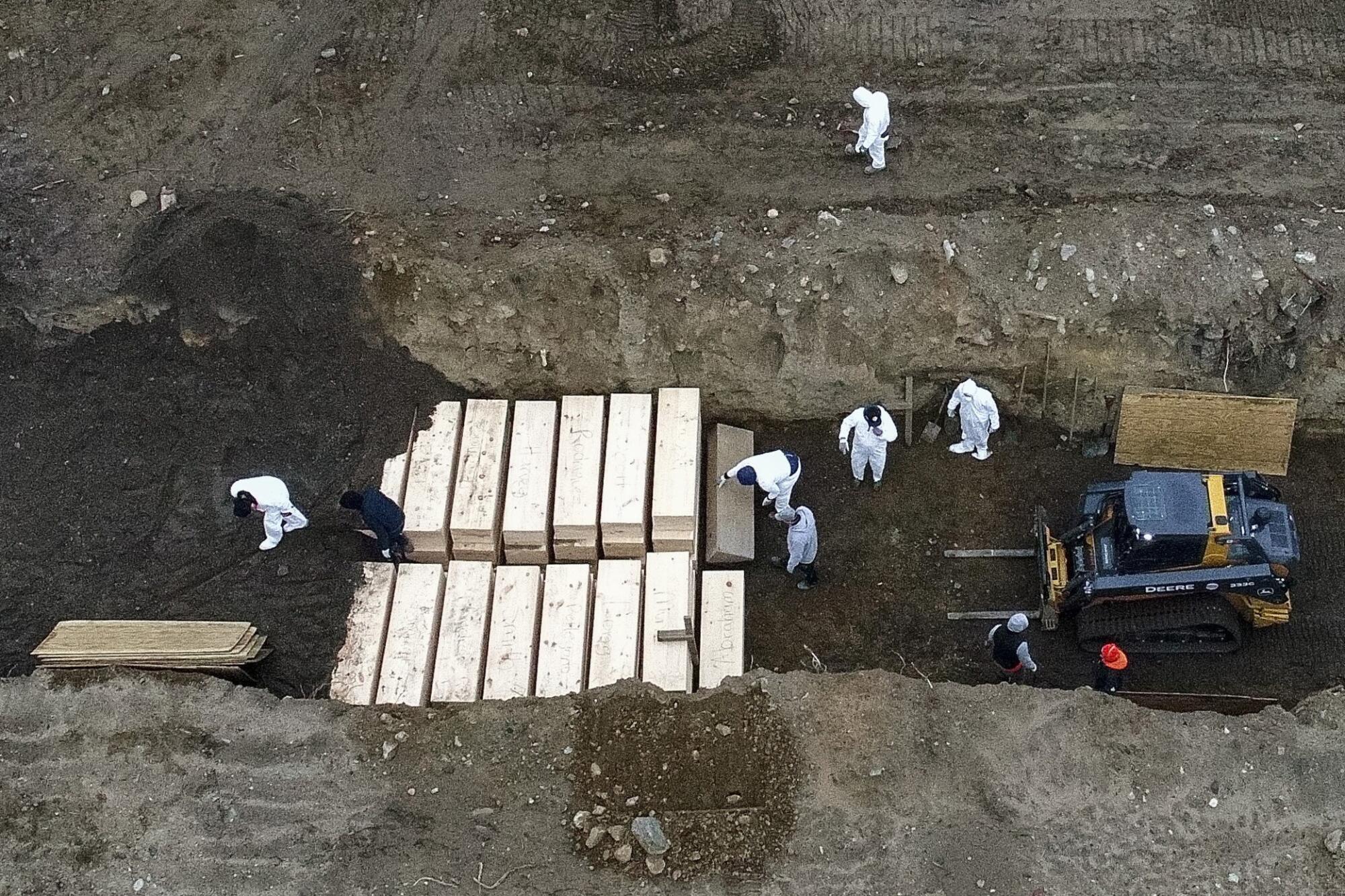 Aerial view of workers burying bodies in a trench.