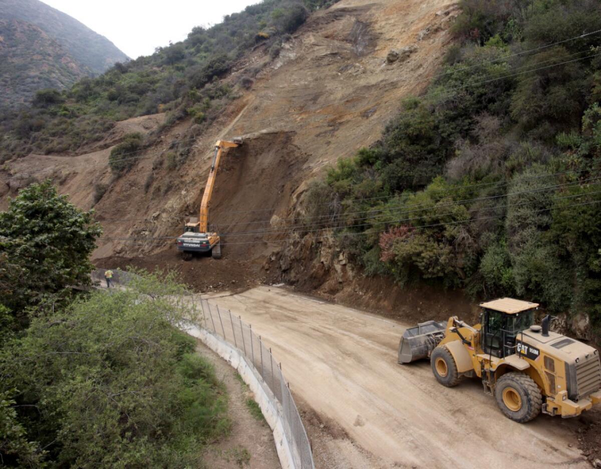 Heavy construction equipment is seen on a landslide next to a mountain road.