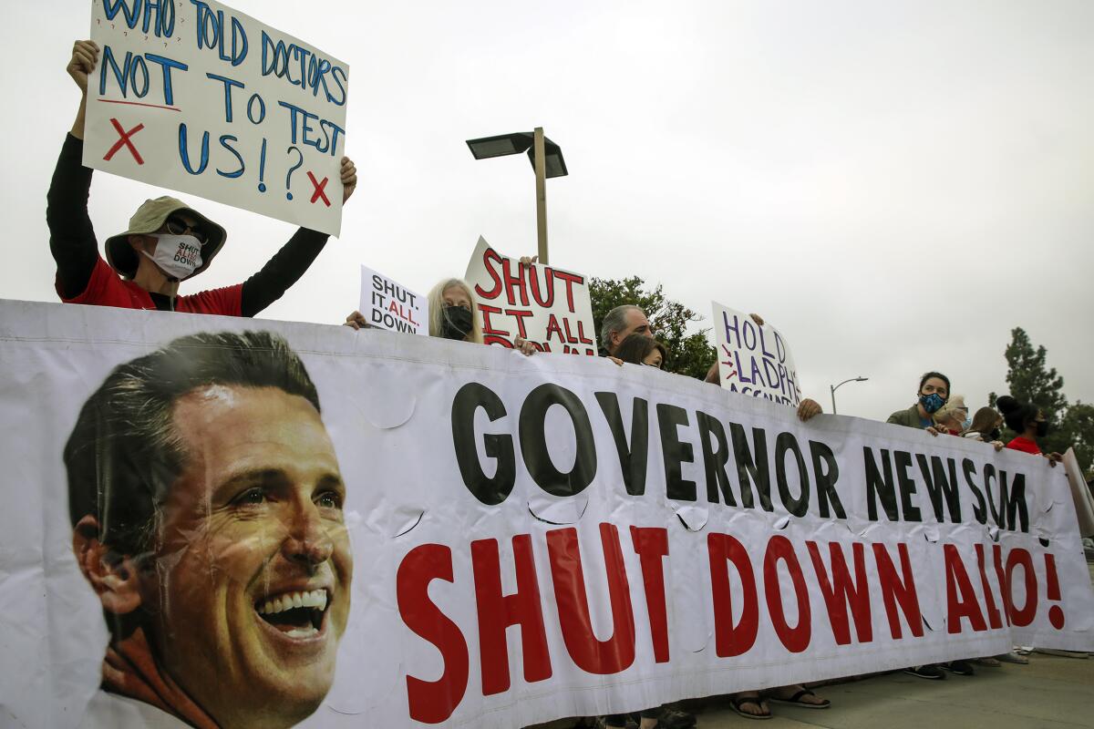 A person holding a sign stands above a banner reading: "Governor Newsom, shut down Aliso!"