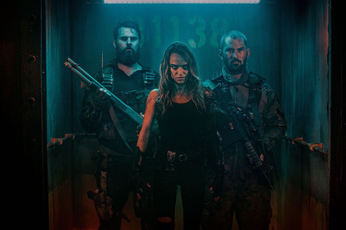 A woman and two heavily-armed men in an open elevator in the movie "Wyrmwood: Apocalypse."