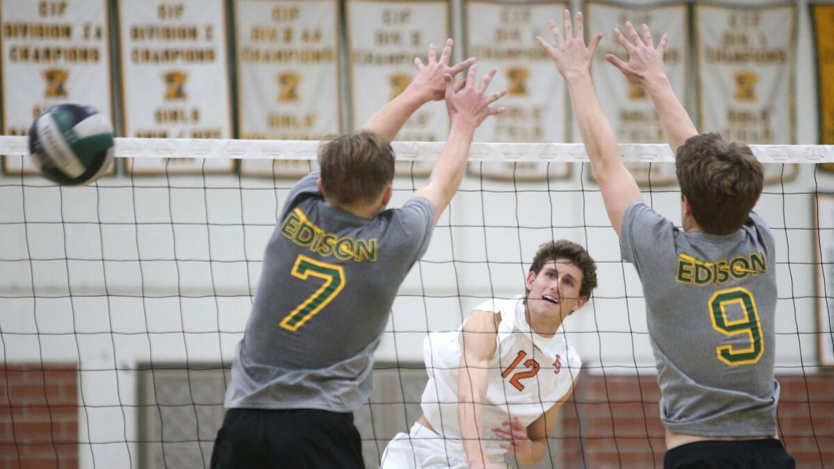 Huntington Beach High middle blocker Mitchell Bollinger hits past Edison's James Carpenter (7) and Austin Pratt (9) during the Orange County Championships tournament at Edison High on March 16.