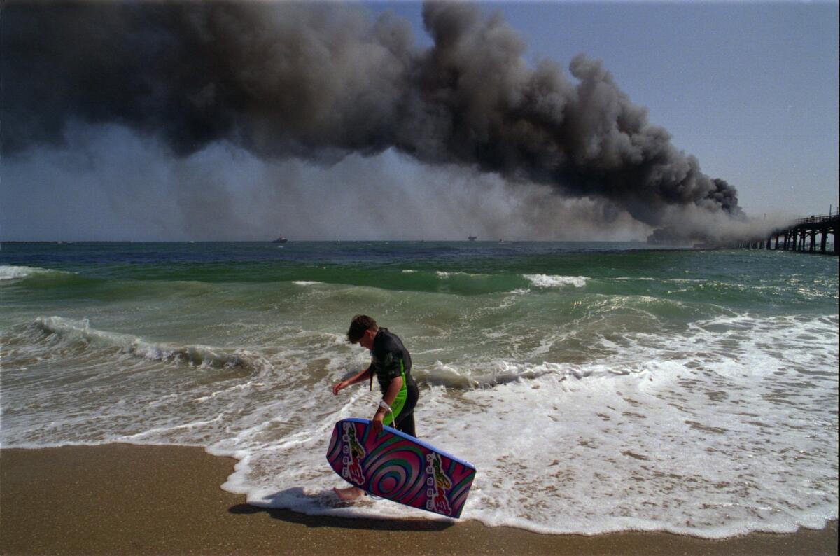 A man walks along the beach as smoke billows from Seal Beach Pier after a fire broke out on May 21, 1994.