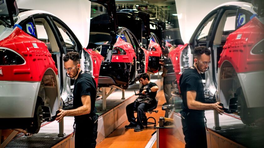 A worker is reflected in a computer screen as he and others assemble cars on Tesla's factory in Fremont, Calif., in 2015.