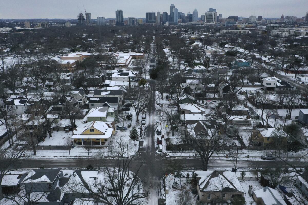 Aerial view of a snowy residential neighborhood, with the high rises of a business district in the background