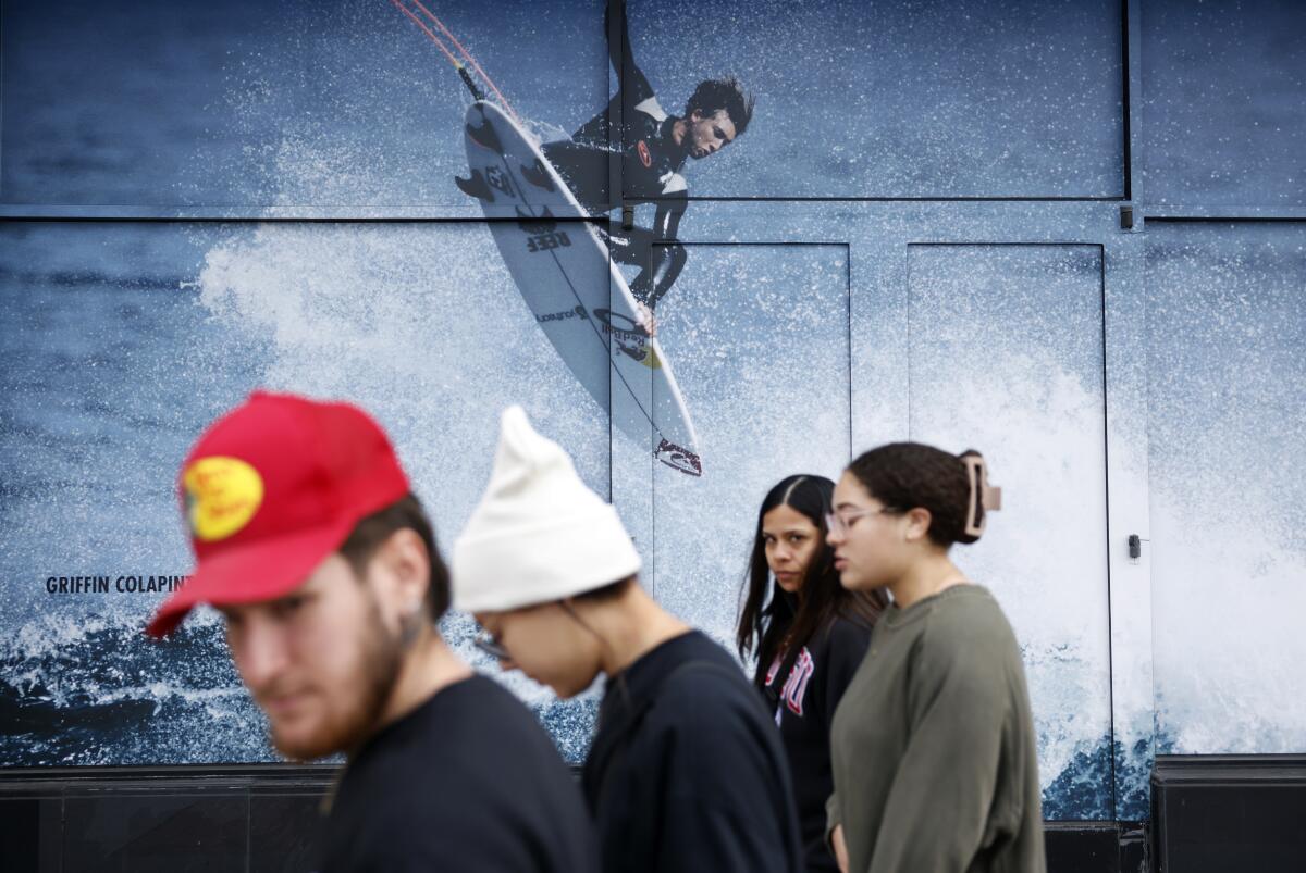 Four people pass a store bearing a large image of a surfer on a board 