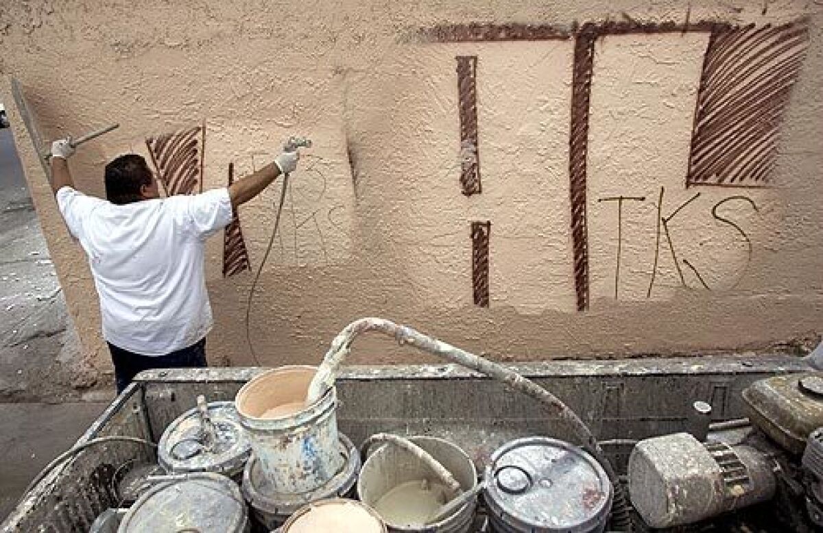 Martin Magdaleno, who works for a graffiti removal company, paints over graffiti on the side of a garage, in the Florence-Firestone area of Los Angeles County, Wednesday.