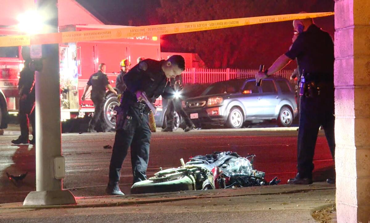 First responders stand near a smashed motorcycle on its side on the road at night