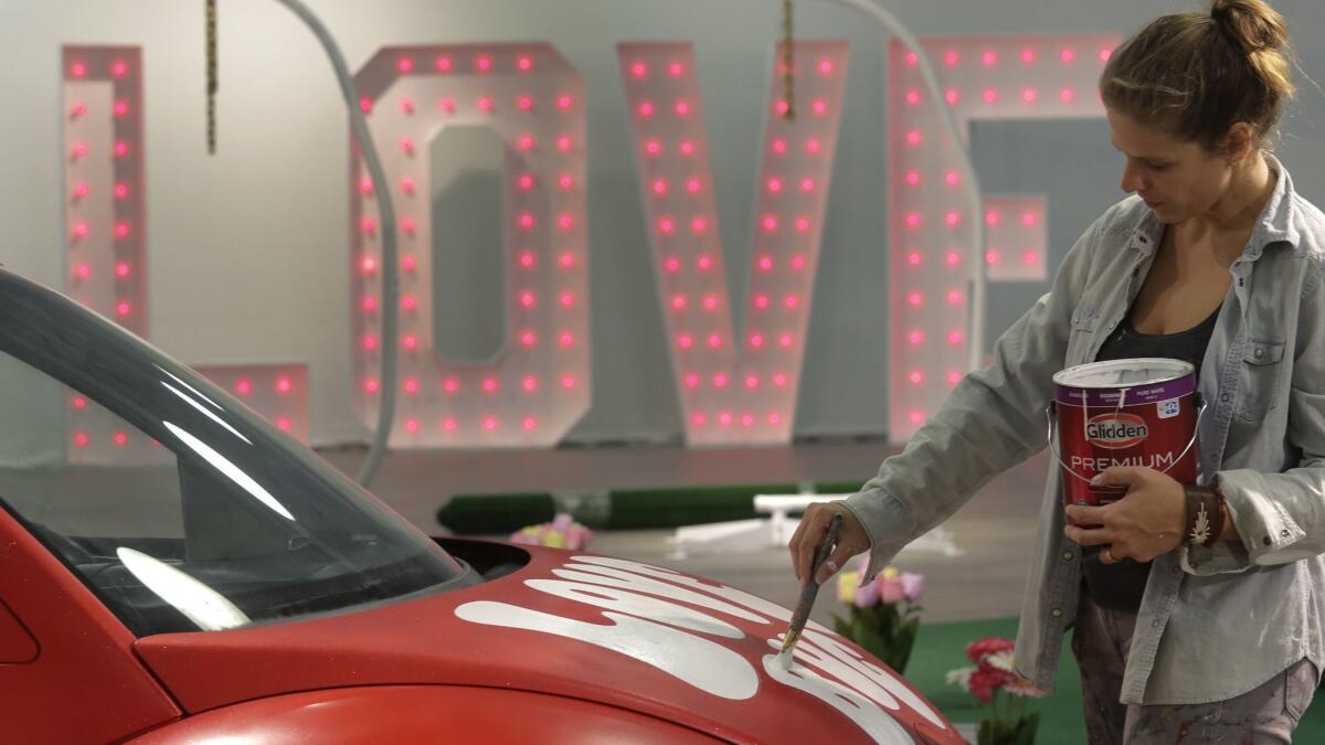 Hanna Daly paints the words Love Bug on a red Volkswagen Beetle during final preparations Thursday morning for the pop-up exhibition "Museum of Wha? Love Tour," which opened on Valentine's Day evening in Encinitas.
