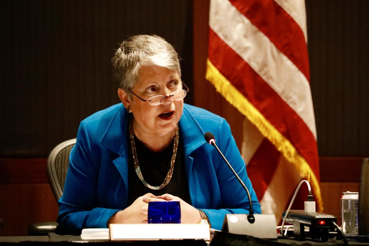 Janet Napolitano speaks into a microphone while sitting a desk 