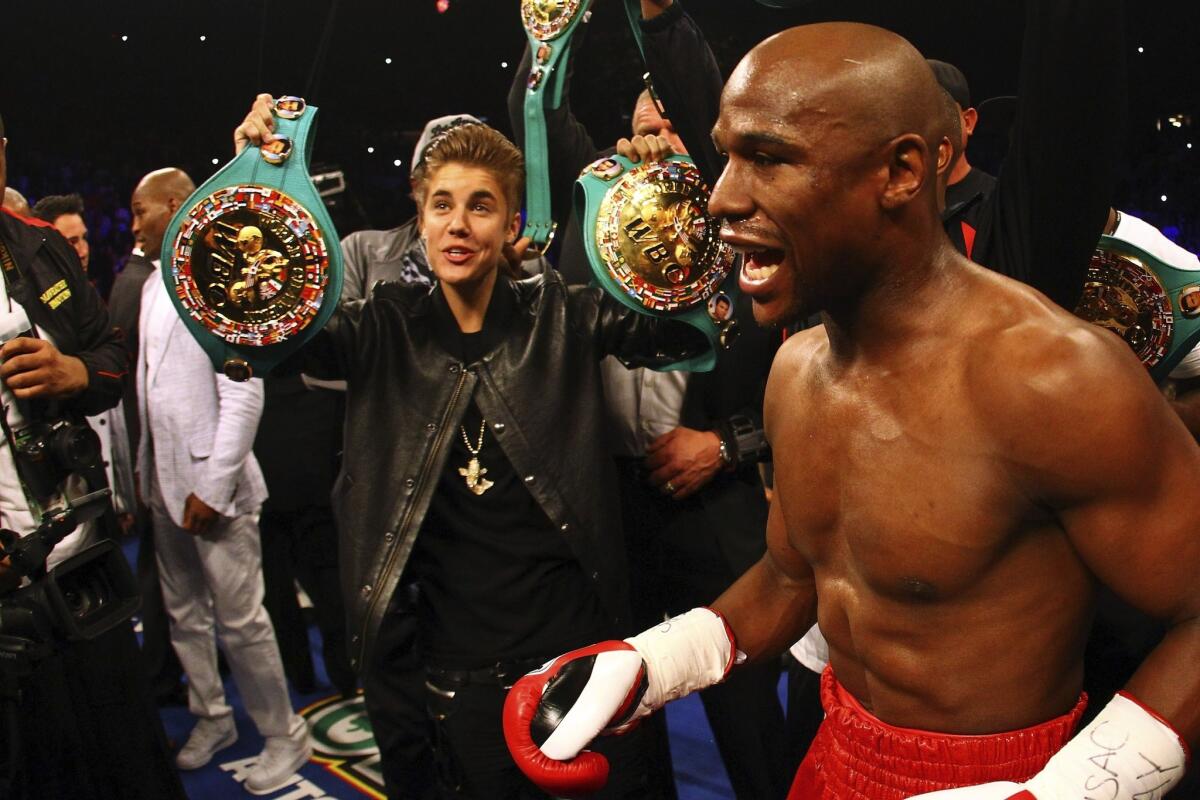Justin Bieber holds up belts for unbeaten Floyd Mayweather Jr. before his May 2012 fight against Miguel Cotto in Las Vegas. Mayweather is now teaching Bieber how to box.