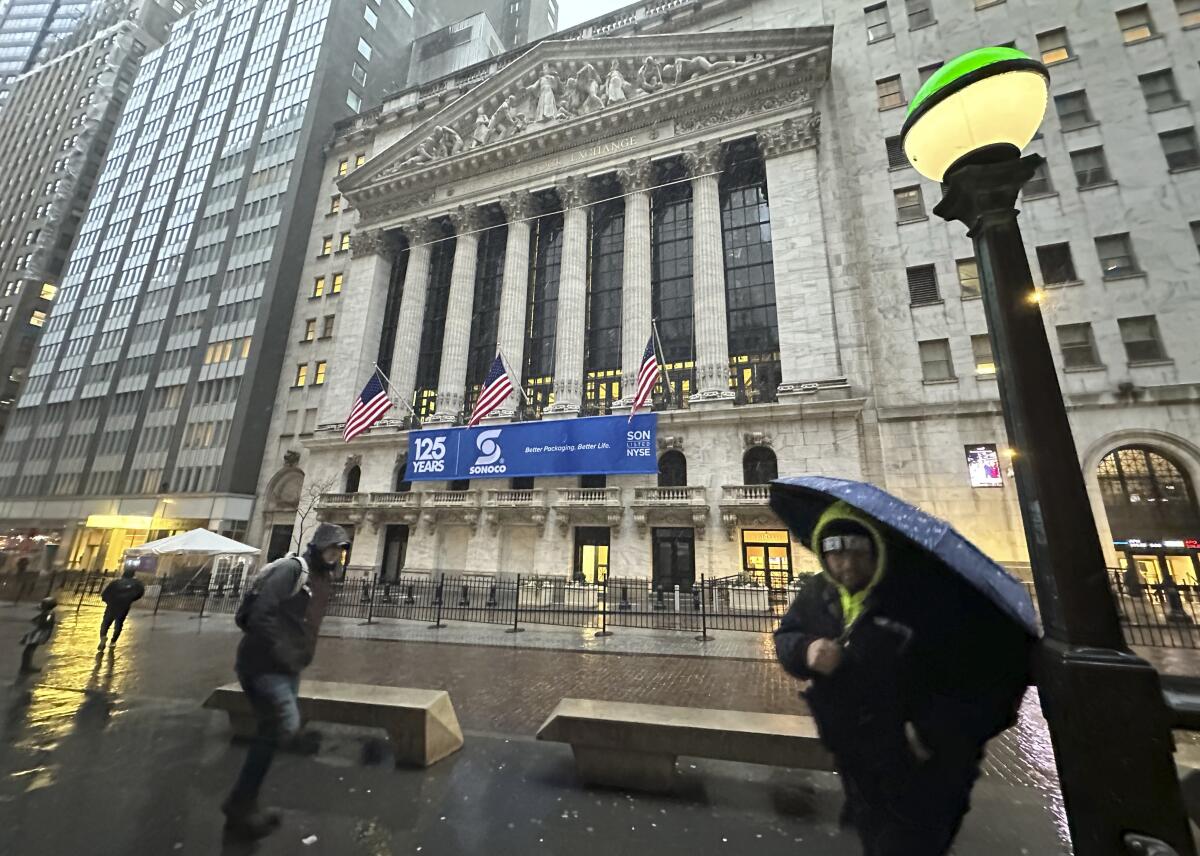 People walk by the New York Stock Exchange as snow falls.