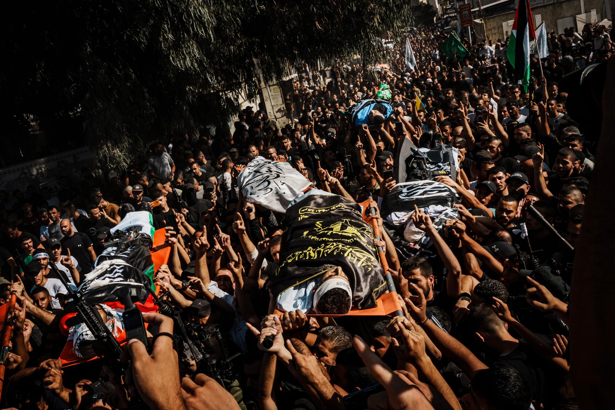 Hands are raised to carry the bodies of the dead wrapped in cloth at a mass funeral.