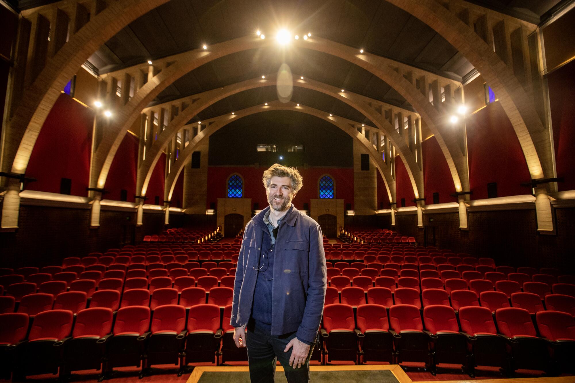 A man stands on a stage in front of rows of red theater seats