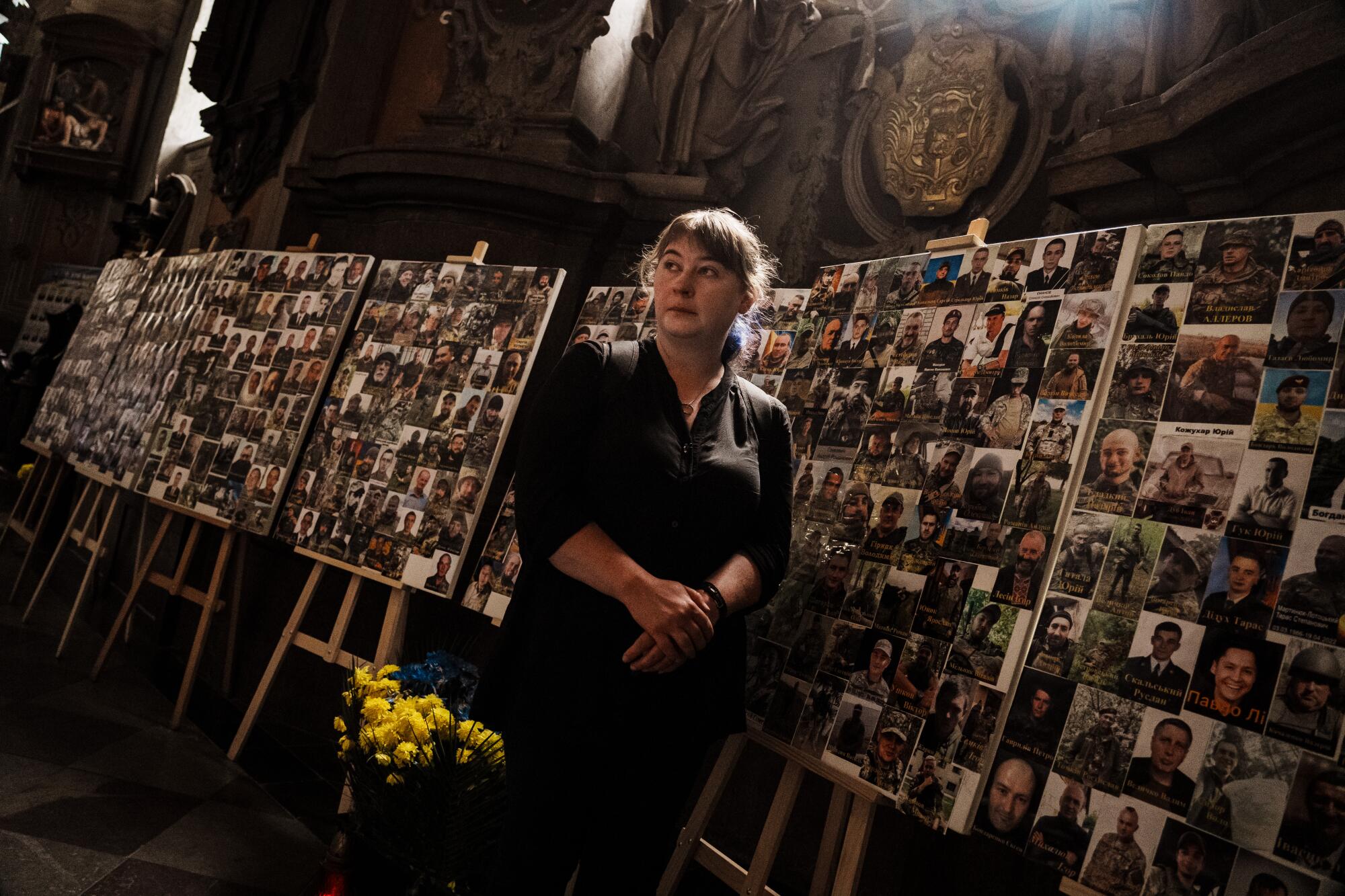 A woman stands next to one of several boards covered with pictures of people