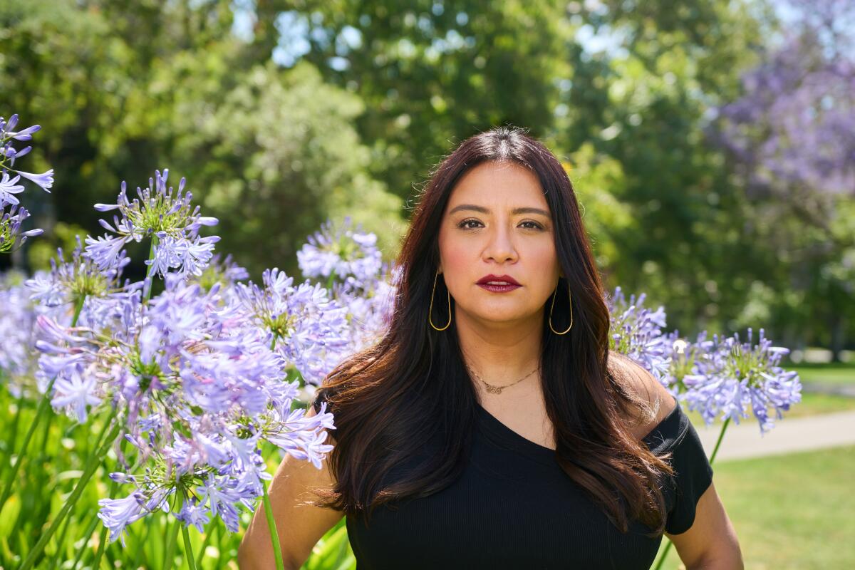 A portrait of Cristela Alonzo standing in a park, surrounded by flowers.