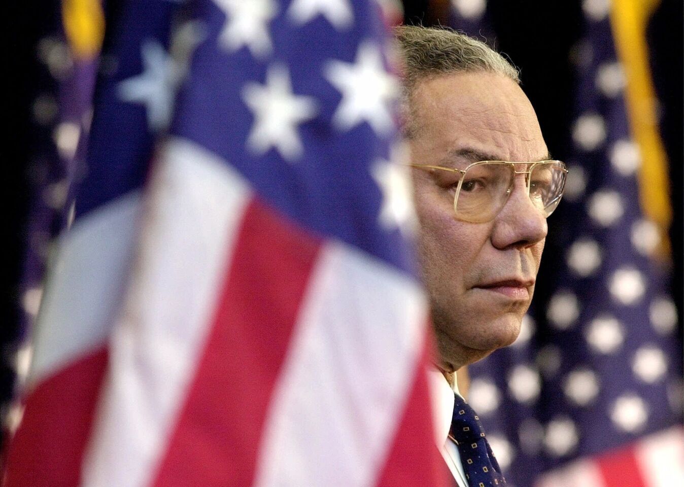Secretary of State Colin Powell is flanked by U.S. flags